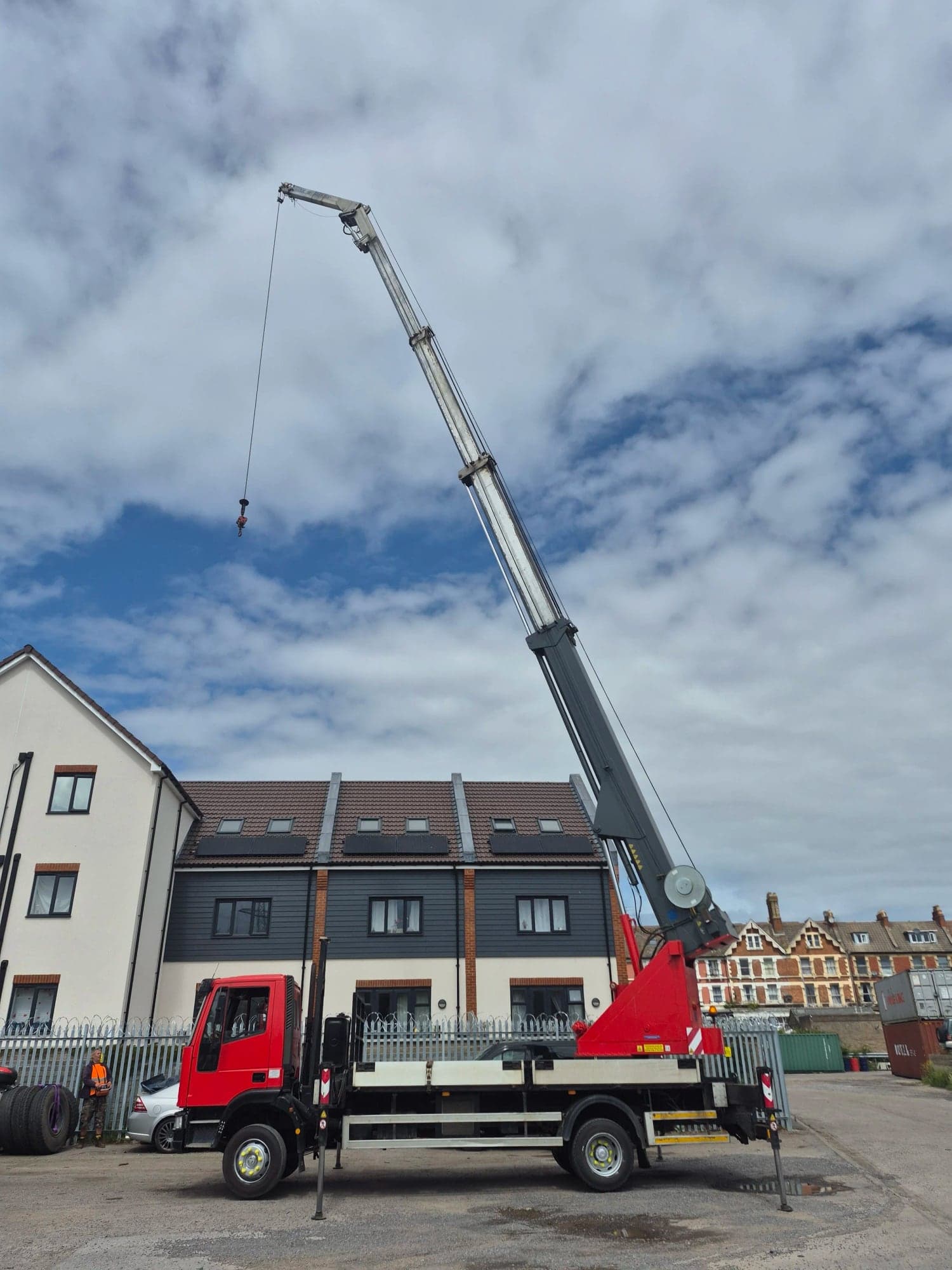 A mobile crane with its boom extended set up in a car park beside a row of houses
